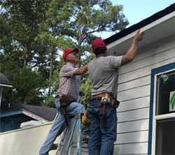 Two volunteers in red BDM hats work on the gutter of a house
