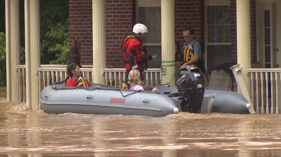 People in boat on a flooded street in front of a house