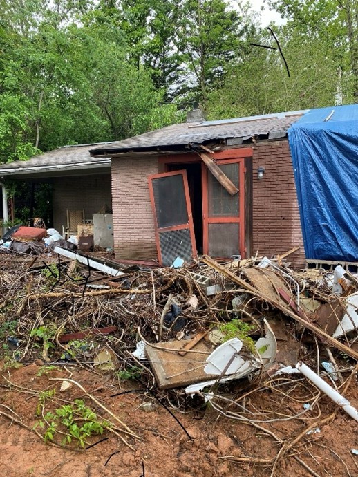 House with door hanging off and a front yard full of rubble