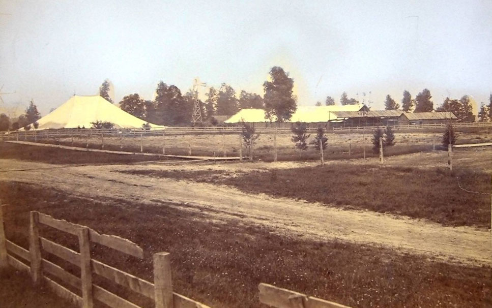 1881 photo of a field, small trees, and large tents.