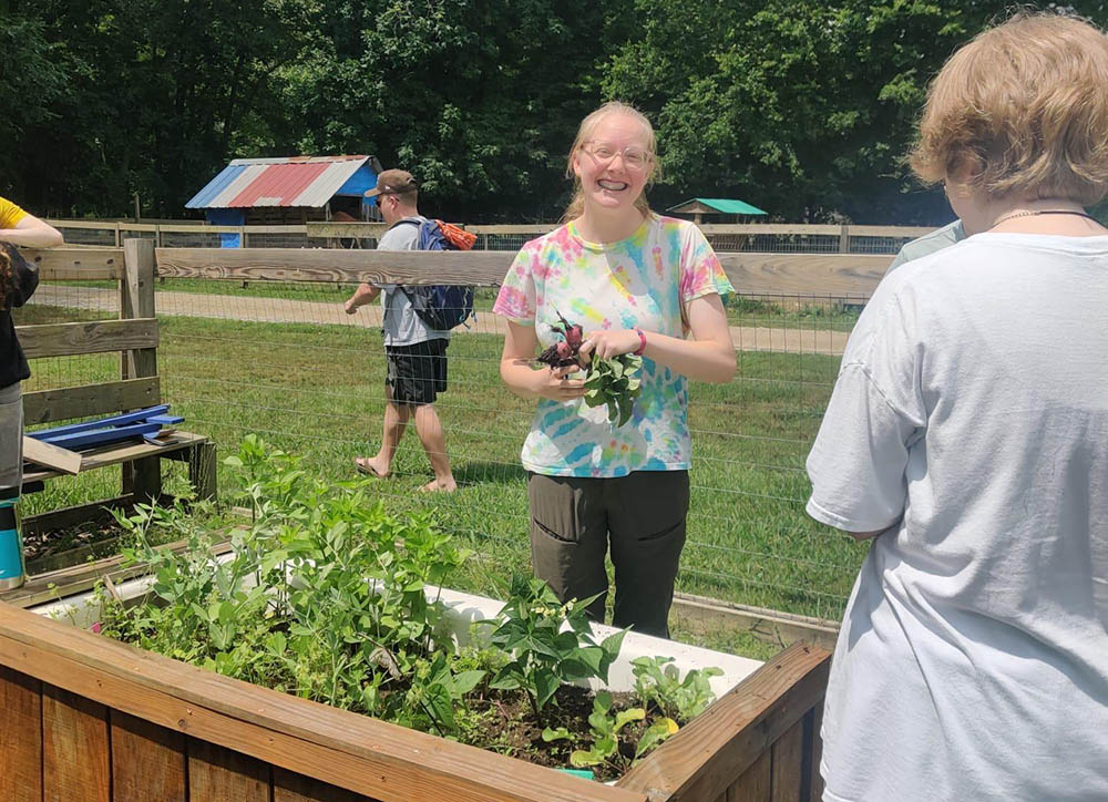 Person holding plants smiling behind a raised garden bed