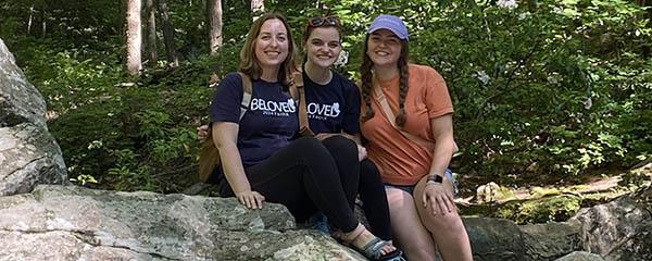 Three people sitting on a rock in the woods