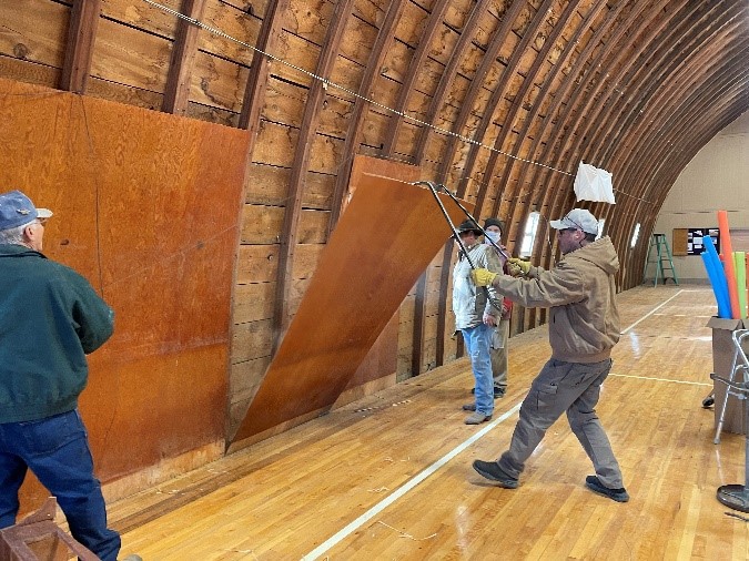 People using crowbars to pull wooden panels off a curved wall.