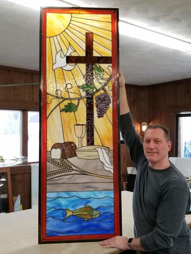 Man holding stained glass window with wun, dove, cross, grapes, bread and cup, basin and town, fish in water, wheat