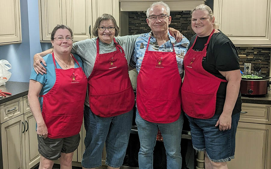Four people in a kitchen wearing red aprons