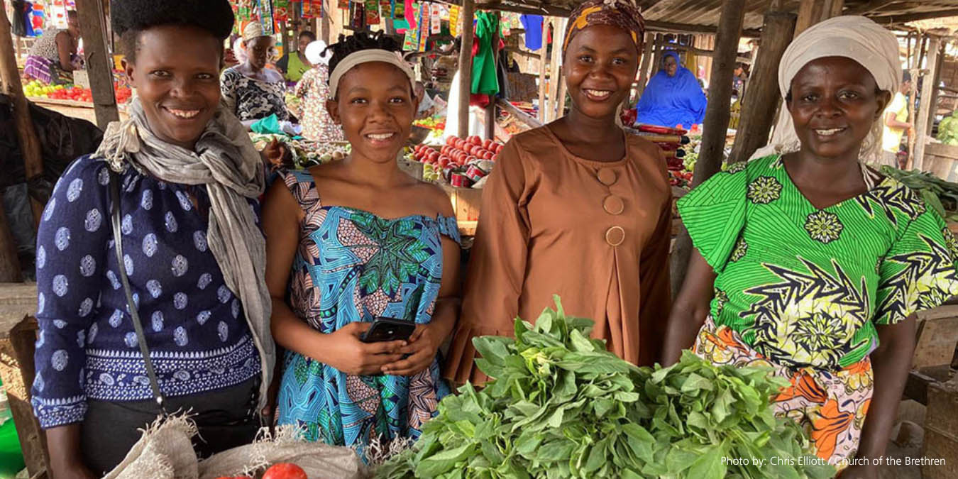 Smiling women behind a pile of produce in a colorful market