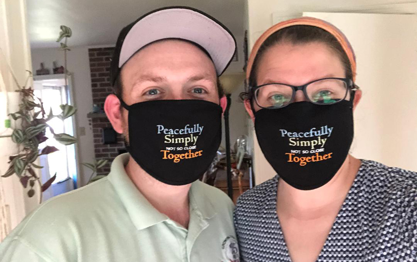Two people wearing masks that say "Peacefully, Simply, Not so close Together"