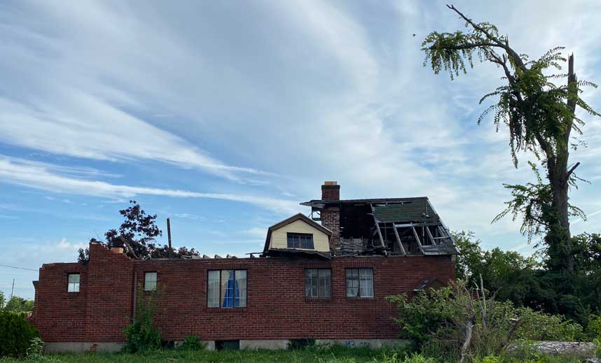 Brick house with destroyed roof next to a broken tree