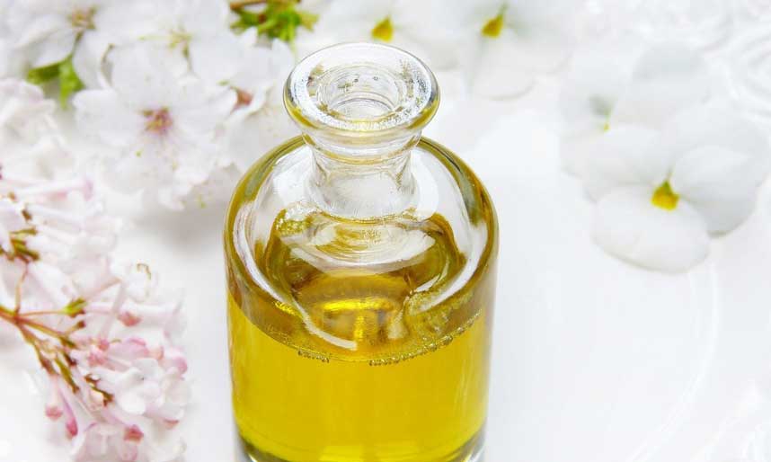 Glass jar of oil with flowers surrounding it