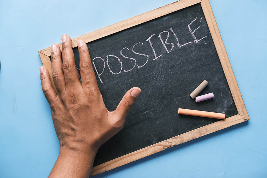 Chalk board that says "impossible" with a hand covering the "im" so that it says "possible"