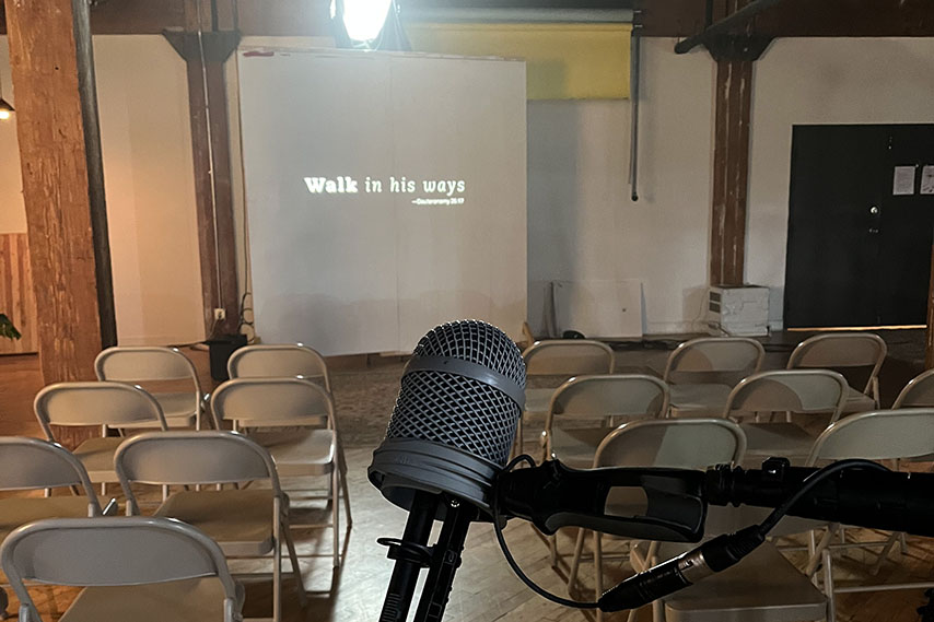Microphone behind empty chairs and a screen that says "Walk in his ways"