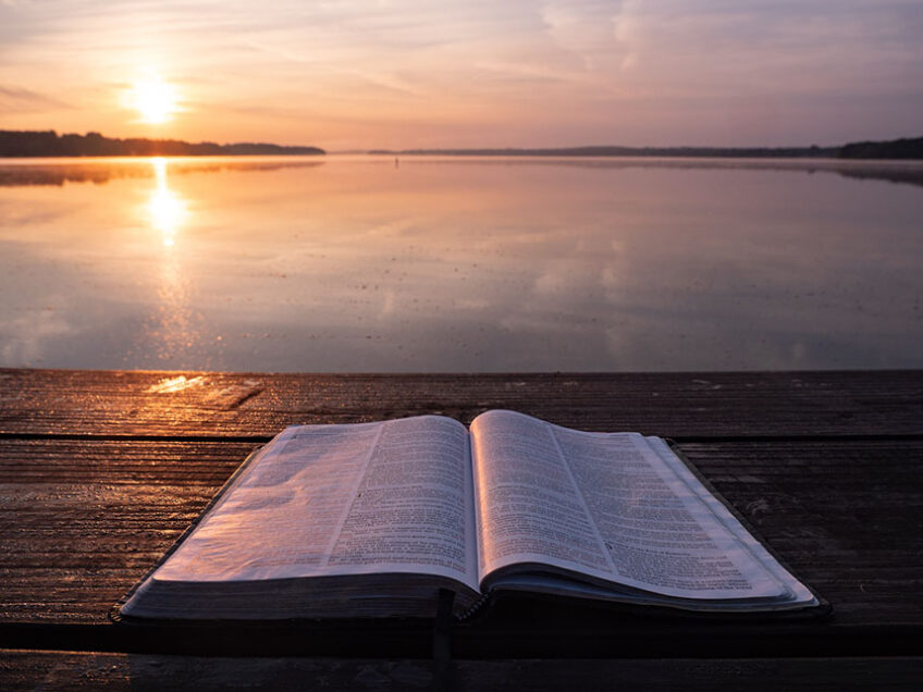 Bible in front of sun setting over lake