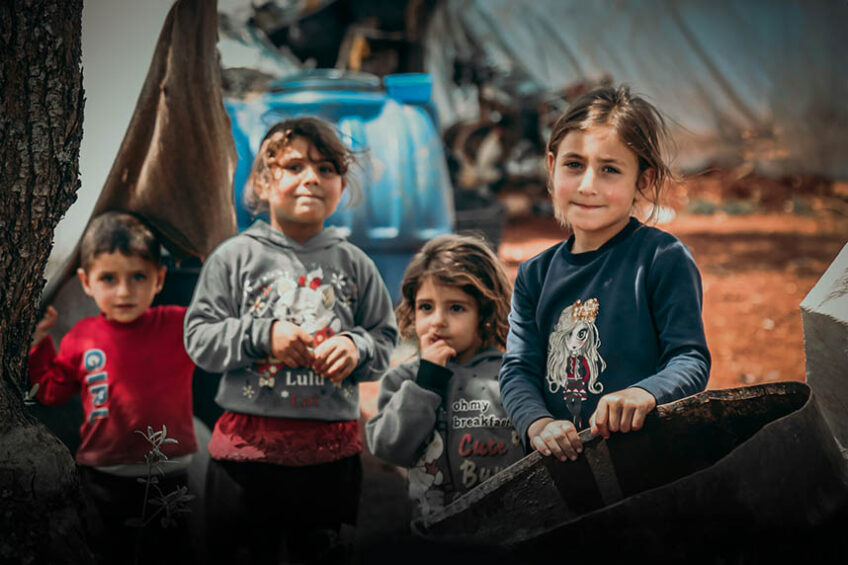 Children standing in front of tents in a refugee camp.
