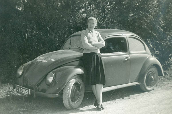Woman leaning on a Volkswagen Beetle.