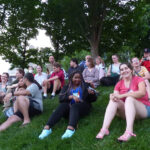 Group of young adults sitting on a grassy hill.