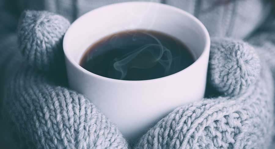 Hands in mittens holding cup of coffee