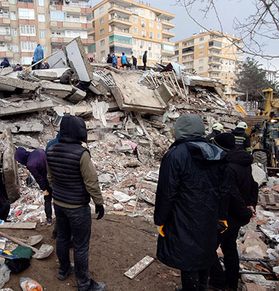 People in winter coats looking at a collapsed building and rubble