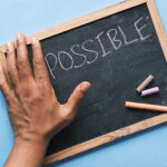 Chalk board that says "impossible" with a hand covering the "im" so that it says "possible"