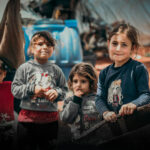 Children standing in front of tents in a refugee camp.